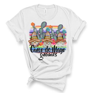 May include: White t-shirt with a colorful graphic of three gnomes wearing sombreros and holding maracas. The gnomes are standing in front of a rainbow striped background with cactus plants. The text "Cinco de Mayo Gnomes" is written below the gnomes.