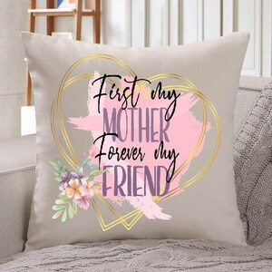 Peut inclure: Un coussin beige avec un motif de c&oelig;ur dor&eacute; et le texte "First my Mother Forever my Friend" en lettres violettes et roses. Le c&oelig;ur est d&eacute;cor&eacute; de coups de pinceau roses et dor&eacute;s et d'un motif floral.