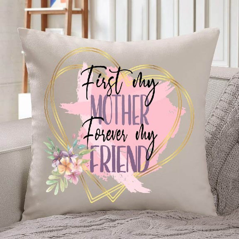 Peut inclure: Un coussin beige avec un motif de c&oelig;ur dor&eacute; et le texte "First my Mother Forever my Friend" en lettres violettes et roses. Le c&oelig;ur est d&eacute;cor&eacute; de coups de pinceau roses et dor&eacute;s et d'un motif floral.