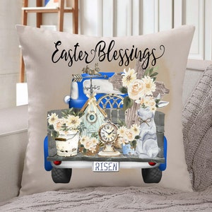 Peut inclure: Un plateau de camion vintage bleu rempli de d&eacute;corations de P&acirc;ques, dont une croix, un nichoir &agrave; oiseaux, une horloge, un lapin et des fleurs. Le plateau du camion a une plaque d'immatriculation qui indique "RISEN". Le camion est sur un oreiller beige avec le texte "Easter Blessings" au-dessus.