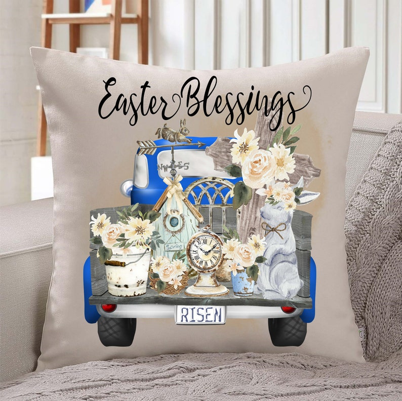 Peut inclure: Un plateau de camion vintage bleu rempli de d&eacute;corations de P&acirc;ques, dont une croix, un nichoir &agrave; oiseaux, une horloge, un lapin et des fleurs. Le plateau du camion a une plaque d'immatriculation qui indique "RISEN". Le camion est sur un oreiller beige avec le texte "Easter Blessings" au-dessus.