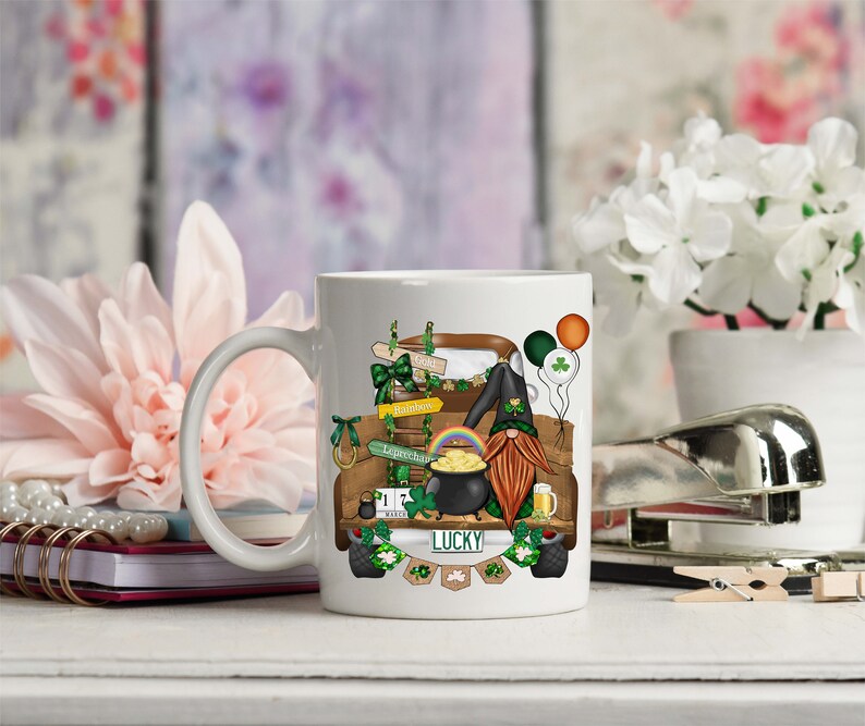 May include: White ceramic mug with a colorful illustration of a gnome driving a truck decorated with shamrocks, rainbows, and a pot of gold. The truck has a license plate that says "LUCKY".