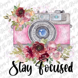 May include: A pink vintage camera with a lens and a floral arrangement of red, pink, and white flowers. The text "Stay Focused" is written below the camera.