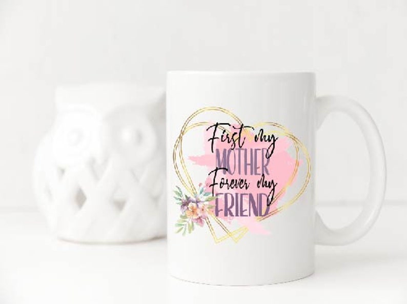 Peut inclure: Une tasse en c&eacute;ramique blanche avec un motif de c&oelig;ur dor&eacute; et le texte "First my Mother forever my Friend". Le c&oelig;ur est rempli d'un motif aquarelle rose et d'une illustration florale.