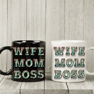May include: Two coffee mugs with the text "Wife Mom Boss" in floral letters. One mug is black and the other is white.