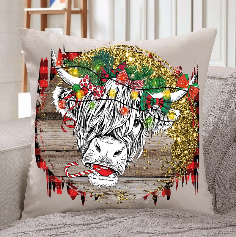 May include: A white and black Highland cow with a red and green tartan background. The cow is wearing a Christmas wreath with red bows and lights. The background is a rustic wood texture with gold glitter.