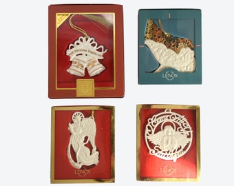 May include: Four Lenox Christmas ornaments in red and gold boxes. The ornaments are white porcelain and feature a bell, an angel, and a sleigh. The boxes have the Lenox logo and the words "Our First Christmas Together 2001" on the front.