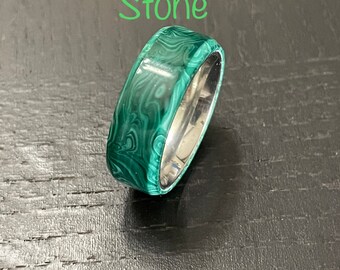May include: A green malachite stone ring set in a silver band. The ring is on a dark wood surface. "Malachite True Stone" is written in green text above the ring.