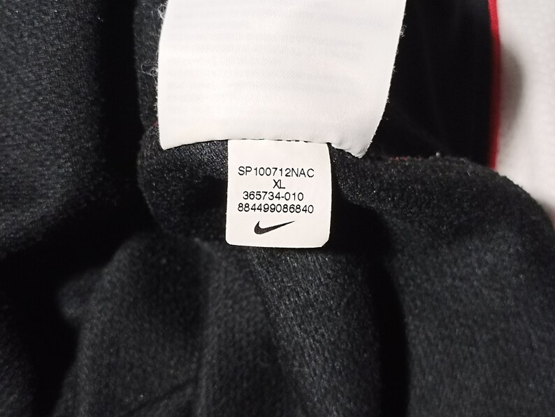 Puede incluir: Una etiqueta blanca con texto negro y un logotipo Nike swoosh. La etiqueta dice "SP100712NAC XL 365734-010 884499086840".
