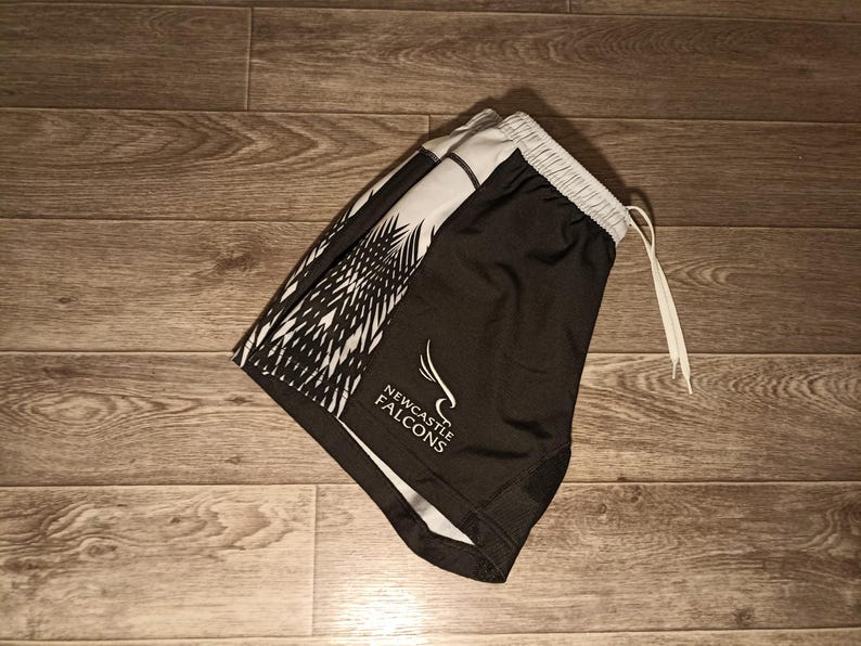 May include: Black and white athletic shorts with a white and black geometric pattern and the words "NEWCASTLE FALCONS" in white text.