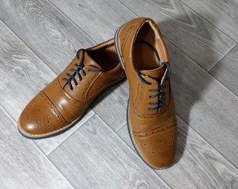 May include: A pair of brown leather lace-up shoes with a brogue design. The shoes have a dark brown sole and black laces.