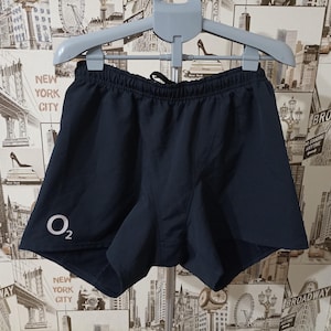 May include: Navy blue athletic shorts with a drawstring waist. The shorts have a white "O2" logo on the left leg. The shorts are hanging on a gray hanger.