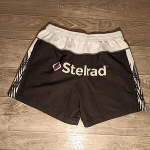 May include: Black and white athletic shorts with a white waistband and a white logo that says "Telrad" on the front.
