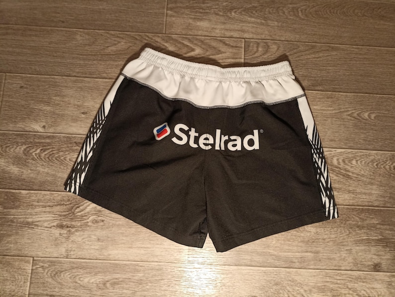 May include: Black and white athletic shorts with a white waistband and a white logo that says "Telrad" on the front.