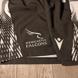 May include: Black and white athletic shorts with a white logo that says "NEWCASTLE FALCONS" and a white chevron design on the side.