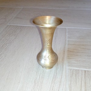 May include: A silver vase with an ornate design. The vase has a round base and a narrow neck.