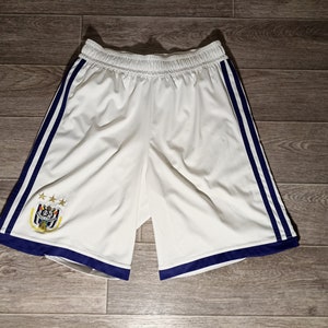 Puede incluir: Pantalones cortos deportivos blancos con rayas azules y blancas a los lados. Los pantalones cortos tienen una cintura azul marino y un pequeño logotipo bordado en la pierna izquierda.