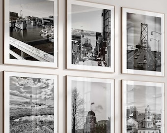 May include: A sectional sofa with beige and brown cushions, a set of three round dark metal coffee tables, and a light-colored armchair. Six black and white framed photographs of cityscapes and landscapes are arranged on the wall above the sofa.