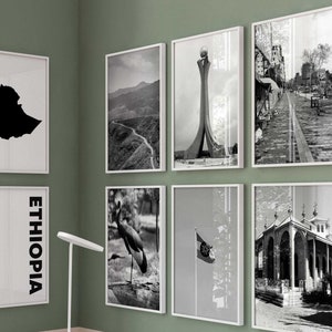 Puede incluir: Un escritorio blanco con tres cajones y una silla blanca delante. El escritorio tiene un portátil, gafas y un jarrón con flores secas encima. Hay seis imágenes enmarcadas en blanco y negro en la pared detrás del escritorio. Las imágenes muestran un mapa de Etiopía, un pájaro, una bandera, un edificio y otros dos paisajes.