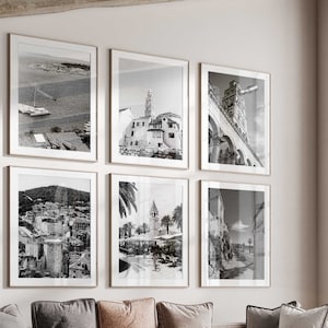 Könnte beinhalten: Ein Wohnzimmer mit einem Ecksofa, einem Couchtisch und einem Sessel. Die Wände sind in einem hellen Beige gestrichen und an der Wand hängen sechs schwarz-weiße gerahmte Fotografien von Stadtansichten. Der Raum hat ein großes Fenster mit Blick auf Bäume im Freien.