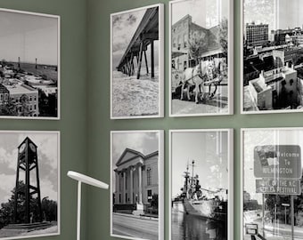 May include: A home office with a white desk and a white chair. The desk has three drawers and a laptop on top. There are six black and white framed photos on the wall behind the desk. The photos are of various scenes in Wilmington, North Carolina. There is a vase with dried flowers and a plant in the corner of the room.