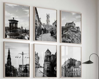May include: A gallery wall set of six black and white framed prints featuring architectural city scenes, including a monument, a stone street, and a castle, arranged in two rows of three above a light gray curved sofa and a round coffee table.