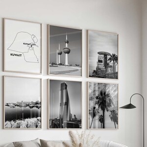 May include: A set of six framed wall art prints featuring black and white photography of Kuwait landmarks and a map of Kuwait with the text Kuwait and Kuwait City, arranged in a grid pattern on a white wall above a light grey curved sofa.