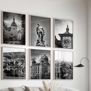 May include: A living room interior with a white sofa, two armchairs, a coffee table, and a floor lamp. Six black and white framed photographs of cityscapes and a statue are displayed on the wall.