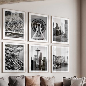May include: A modern living room with a sectional sofa, a coffee table, and an armchair. The walls are decorated with black and white photographs of the Seattle skyline, including the Space Needle.