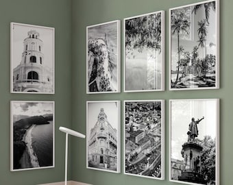 Op de afbeelding: Een wit bureau met drie lades, een witte lamp en een witte stoel, geplaatst tegen een muur met acht zwart-wit ingelijste prints van architecturale en kustlandschappen. Op het bureau liggen een laptop en een witte bril.