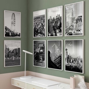 May include: A white desk with three drawers and a white chair in front of it. The desk is against a wall with a green top half and a pink bottom half. There are eight black and white framed photos of cityscapes hanging on the wall above the desk.