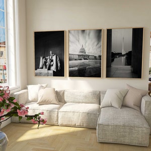 May include: Three black and white framed photographs of Washington D.C. landmarks. The photos are hung on a white wall above a light gray sectional sofa. The sofa has a light gray throw pillow and a white throw pillow.