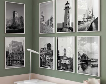 May include: A gallery wall arrangement of seven black and white framed prints featuring architectural landmarks, lighthouses, and coastal scenes. Each rectangular print is encased in a thin white frame, displayed in a grid pattern on a green wall.