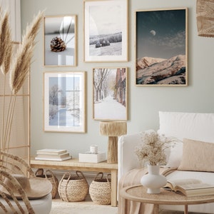 May include: A living room interior with a white couch, a wooden coffee table, and a wooden bench with three woven baskets. There are five framed pictures on the wall, all with winter scenes. The room is decorated in a neutral color palette with beige and brown tones.