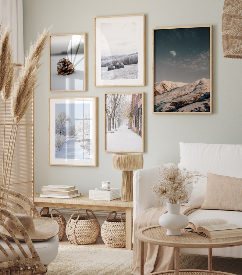 May include: A living room interior with a white couch, a wooden coffee table, and a wooden bench with three woven baskets. There are five framed pictures on the wall, all with winter scenes. The room is decorated in a neutral color palette with beige and brown tones.