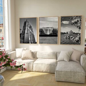 May include: A living room interior with a sectional sofa, three black and white framed photographs on the wall, and a vase of pink flowers on the floor.