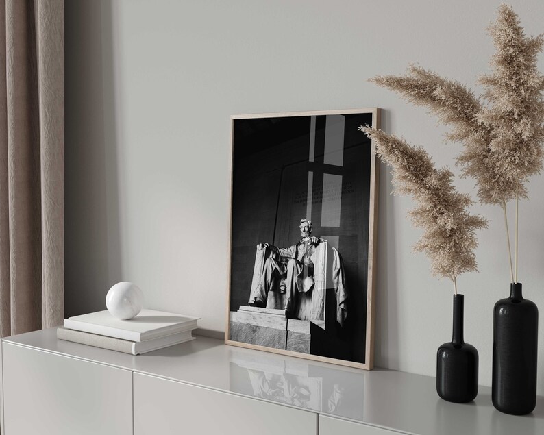 May include: Black and white photograph of a statue of Abraham Lincoln in a frame on a white shelf with two vases of dried pampas grass.