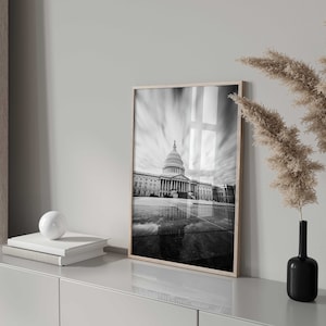 May include: Black and white photograph of the US Capitol building in Washington, D.C. The photo is framed in a simple wooden frame and is hanging on a white wall.