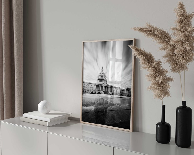 May include: Black and white photograph of the US Capitol building in Washington, D.C. The photo is framed in a simple wooden frame and is hanging on a white wall.