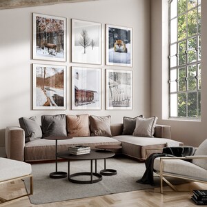 May include: A living room with a sectional sofa, a coffee table, and an armchair. The walls are decorated with framed winter-themed photographs. The room has a large window with a view of trees.