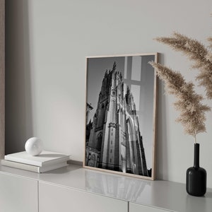 May include: Black and white photograph of a tall, pointed building with intricate details. The photo is framed and hanging on a wall in a modern interior.