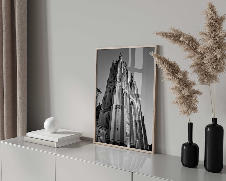 May include: Black and white photograph of a tall, pointed building with intricate details. The photo is framed and hanging on a wall in a modern interior.