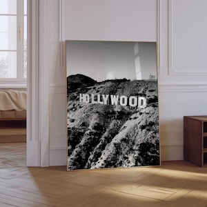 Puede incluir: Impresión en blanco y negro enmarcada del letrero de Hollywood en una ladera. El letrero está en letras mayúsculas blancas. La impresión se muestra sobre un suelo de madera, con una montaña y el cielo de fondo.