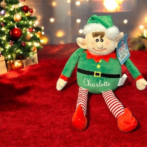 May include: A green plush Christmas elf toy with a red and white striped outfit and a name tag that says "Charlotte".