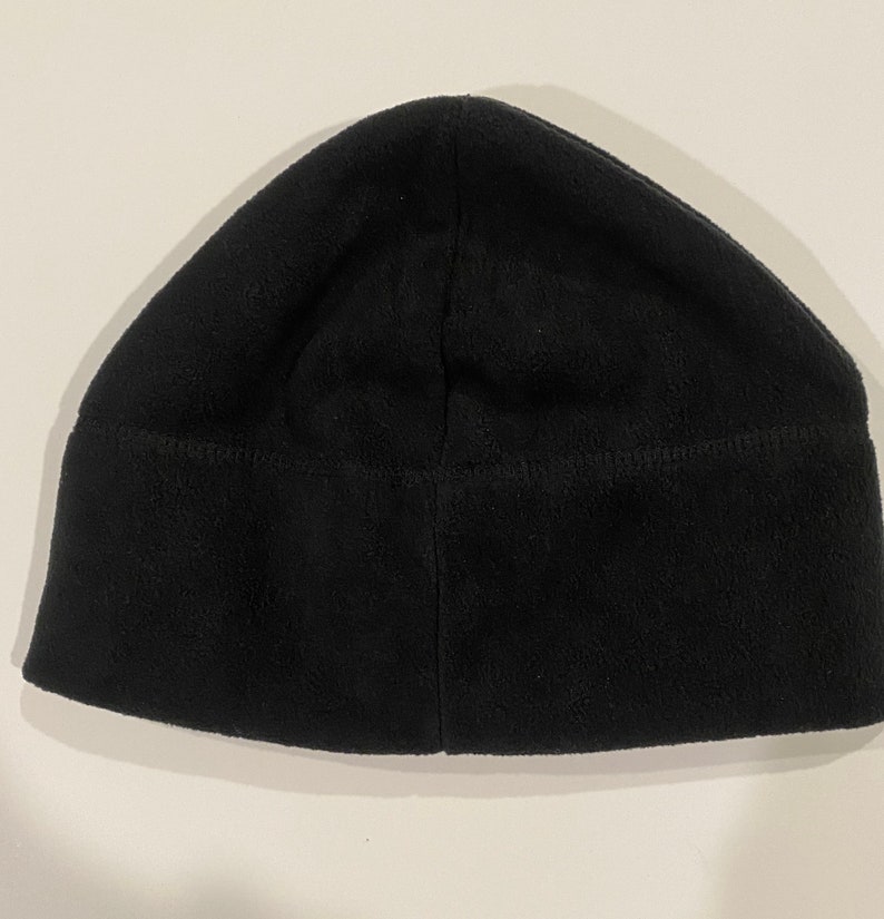Puede incluir: Un gorro de punto negro de forro polar. El gorro est&aacute; doblado por la mitad y la costura es visible.