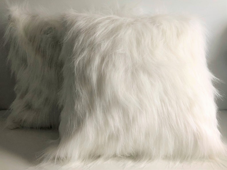 May include: Two white faux fur throw pillows. The pillows are soft and fluffy, and they would be perfect for adding a touch of luxury to any room.