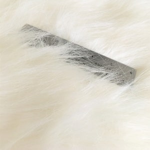 May include: Close-up of a white faux fur fabric with a ruler placed on top. The ruler is marked with inches and shows a measurement of 6 inches.