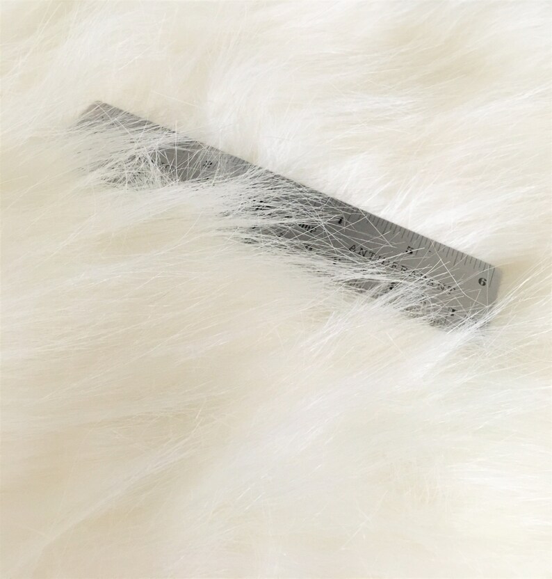 May include: Close-up of a white faux fur fabric with a ruler placed on top. The ruler is marked with inches and shows a measurement of 6 inches.