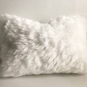May include: A white faux fur pillow with a soft, fluffy texture. The pillow is rectangular and has a smooth, even surface.