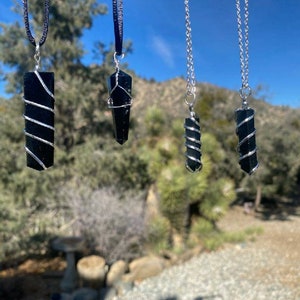 May include: Four black obsidian crystal pendants with silver wire wrapped around them, hanging from black and silver chains against a blue sky background.
